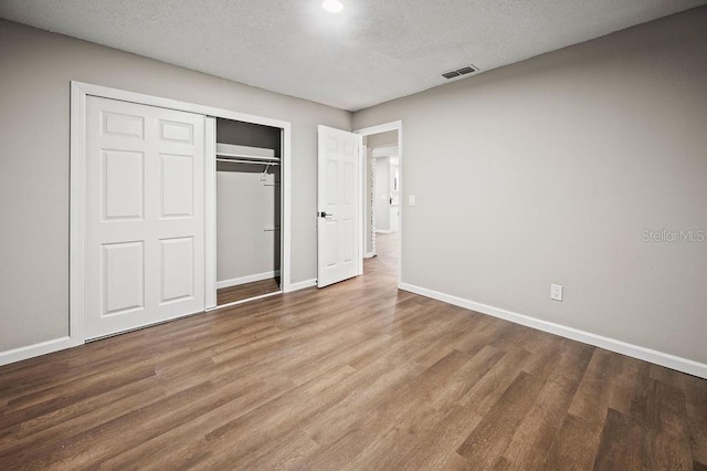 unfurnished bedroom featuring a closet, visible vents, baseboards, a textured ceiling, and wood finished floors