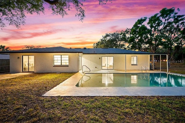 back of house at dusk featuring fence, stucco siding, an outdoor pool, and a patio area