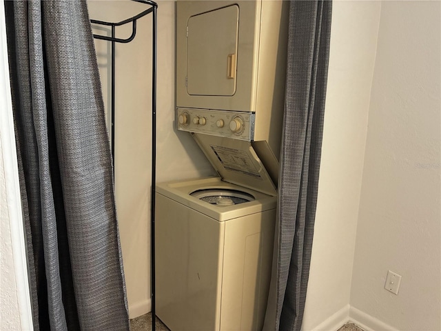 clothes washing area with baseboards, stacked washer and clothes dryer, and laundry area