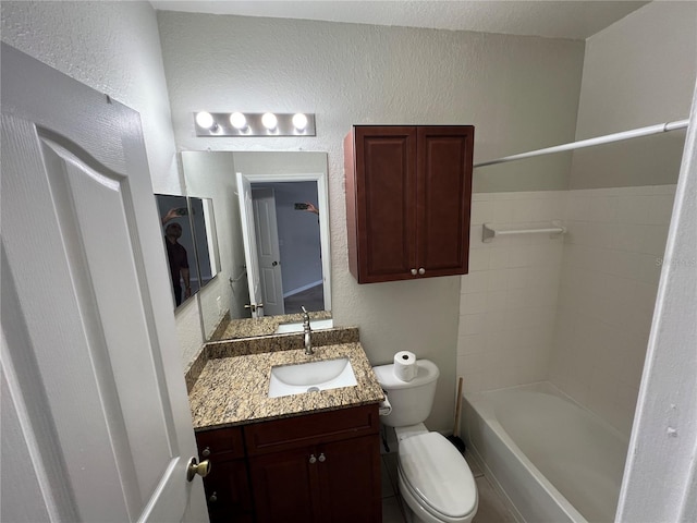 full bath with a textured wall, toilet, vanity, and washtub / shower combination
