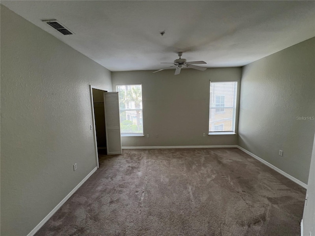 carpeted spare room with healthy amount of natural light, a ceiling fan, baseboards, and a textured wall