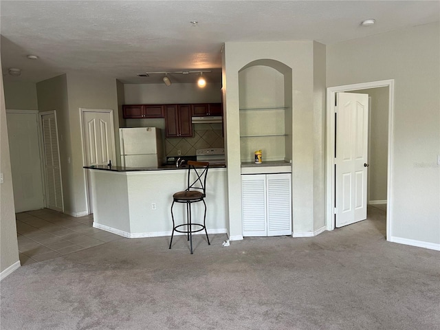 kitchen with freestanding refrigerator, carpet, dark countertops, under cabinet range hood, and a peninsula