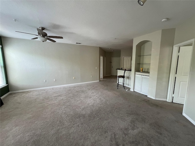 unfurnished living room with carpet flooring, a ceiling fan, and baseboards
