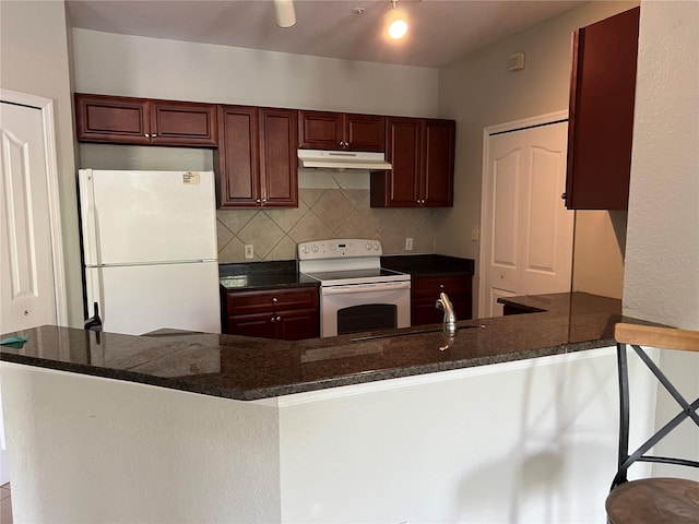 kitchen with white appliances, under cabinet range hood, a sink, backsplash, and a peninsula