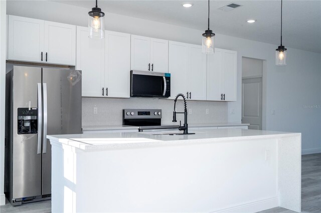 kitchen with hanging light fixtures, an island with sink, stainless steel appliances, light countertops, and visible vents