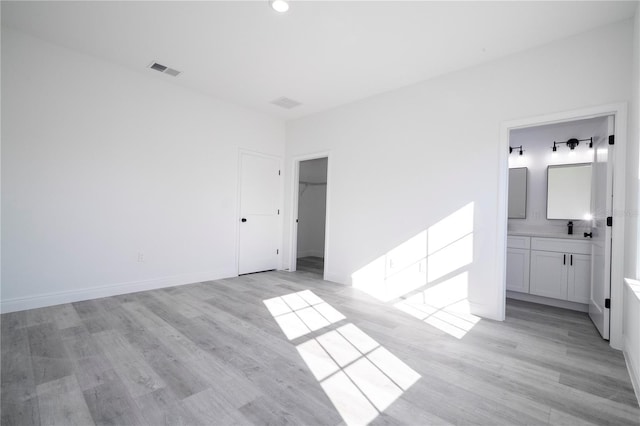 unfurnished bedroom featuring baseboards, ensuite bathroom, visible vents, and light wood-type flooring
