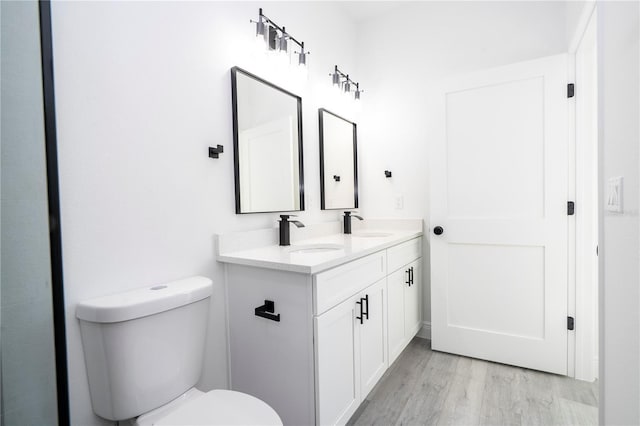 bathroom featuring wood finished floors, a sink, double vanity, and toilet