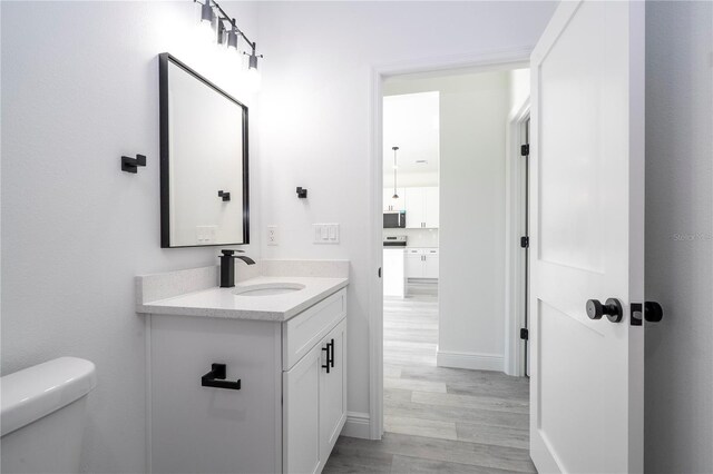 half bathroom with baseboards, wood finished floors, vanity, and toilet