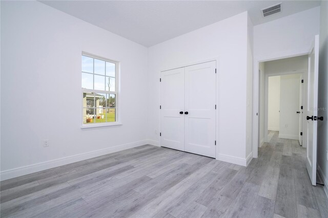unfurnished bedroom featuring light wood-type flooring, baseboards, visible vents, and a closet