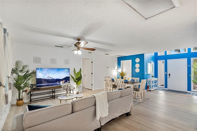 living area with visible vents, a ceiling fan, baseboards, light wood-style flooring, and a textured ceiling