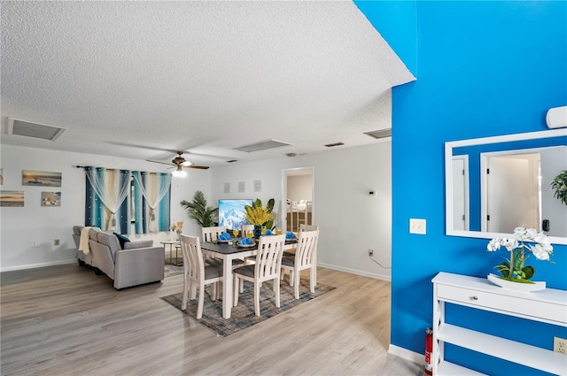 dining space with attic access, a textured ceiling, visible vents, a ceiling fan, and wood finished floors