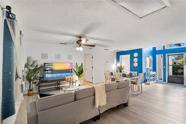living room with ceiling fan, visible vents, wood finished floors, and a textured ceiling