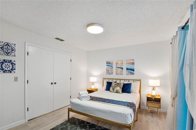 bedroom with baseboards, light wood-style floors, visible vents, and a textured ceiling