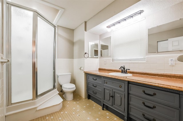 bathroom with tile walls, a shower stall, vanity, tile patterned floors, and toilet
