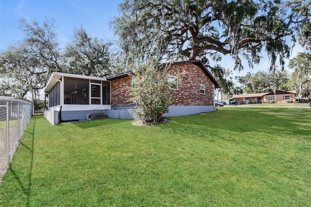 view of side of home with fence, a yard, brick siding, and a sunroom