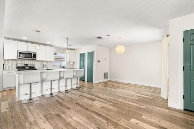 kitchen with light wood-style floors, tasteful backsplash, visible vents, white cabinets, and appliances with stainless steel finishes