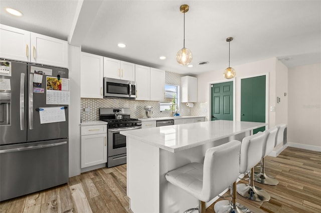 kitchen with white cabinets, tasteful backsplash, appliances with stainless steel finishes, and light wood finished floors