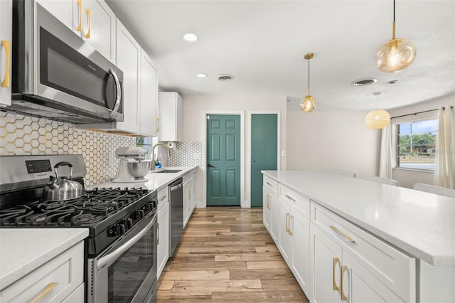 kitchen with a sink, stainless steel appliances, tasteful backsplash, light wood-type flooring, and white cabinetry
