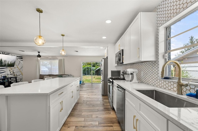 kitchen featuring decorative backsplash, a sink, appliances with stainless steel finishes, open floor plan, and light wood finished floors