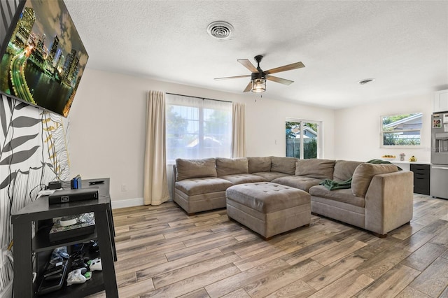 living area featuring light wood-style floors, ceiling fan, visible vents, baseboards, and a textured ceiling