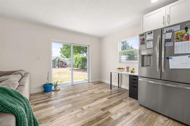 kitchen with light wood-style floors, baseboards, light countertops, white cabinets, and stainless steel fridge with ice dispenser