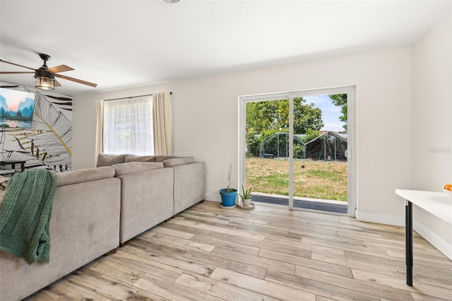 living room with ceiling fan, baseboards, and light wood-type flooring