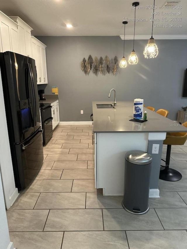 kitchen with an island with sink, freestanding refrigerator, range, white cabinets, and a sink