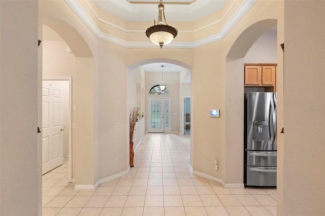corridor featuring a raised ceiling, light tile patterned flooring, ornamental molding, and arched walkways