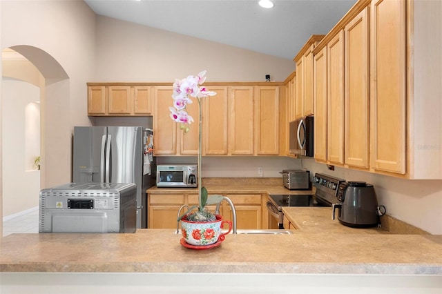 kitchen with arched walkways, light brown cabinets, appliances with stainless steel finishes, and vaulted ceiling