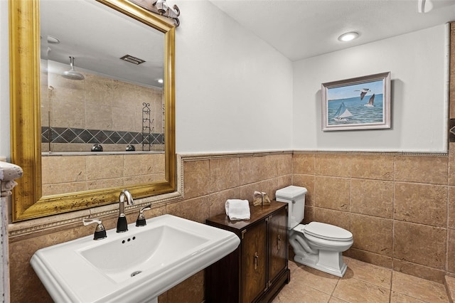full bathroom featuring a tile shower, a sink, visible vents, toilet, and tile walls