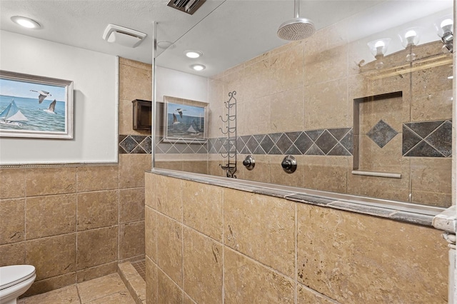 full bathroom with toilet, tile walls, visible vents, and a walk in shower
