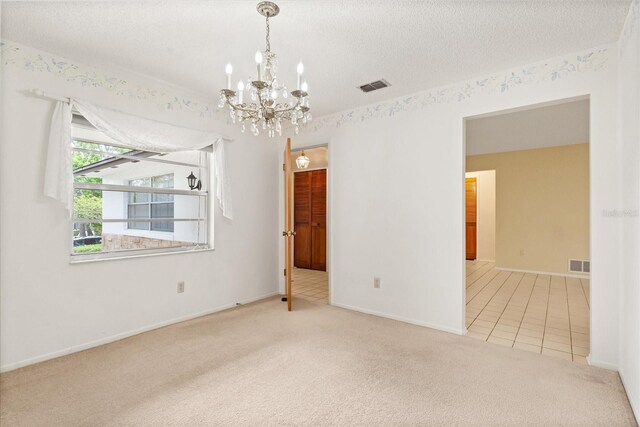 carpeted empty room featuring tile patterned floors, baseboards, visible vents, and an inviting chandelier