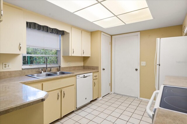 kitchen with light countertops, cream cabinetry, a sink, and white appliances