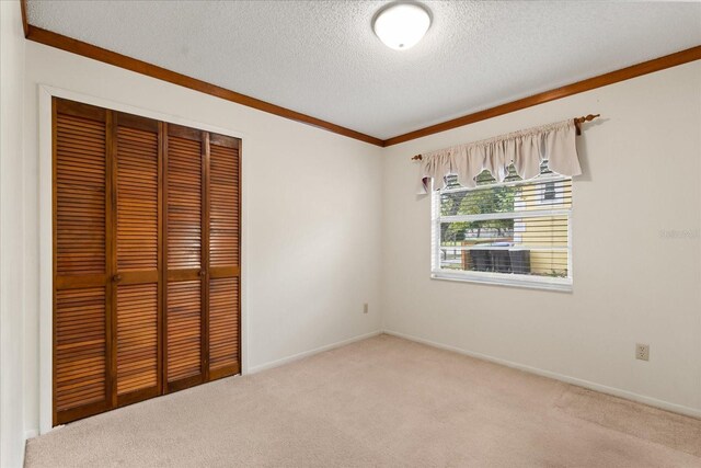 unfurnished bedroom featuring ornamental molding, a closet, baseboards, a textured ceiling, and carpet flooring