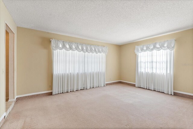 unfurnished room with baseboards, carpet flooring, a wealth of natural light, and a textured ceiling