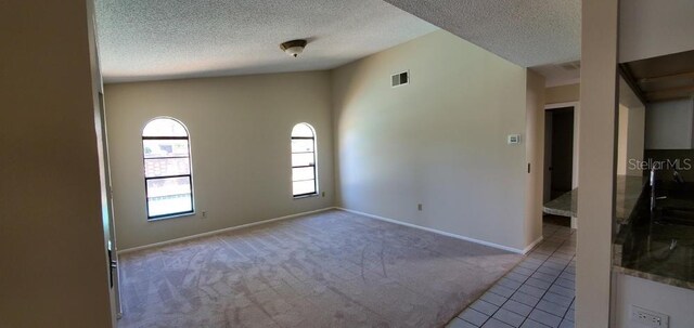 carpeted spare room with a textured ceiling, tile patterned flooring, baseboards, and visible vents
