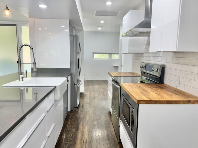 kitchen featuring wall chimney exhaust hood, dark wood-style flooring, butcher block countertops, appliances with stainless steel finishes, and white cabinetry