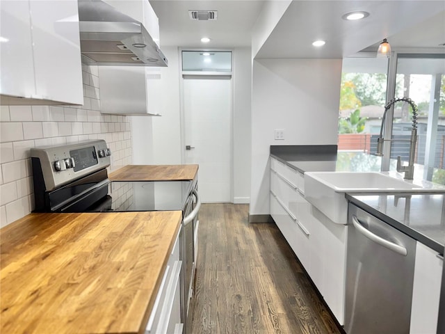 kitchen with wood counters, modern cabinets, stainless steel appliances, wall chimney exhaust hood, and visible vents