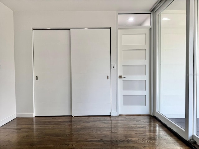 unfurnished bedroom with baseboards, dark wood-style floors, and a closet