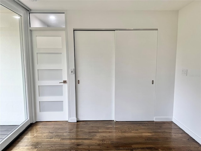unfurnished bedroom with baseboards, dark wood-style flooring, and a closet