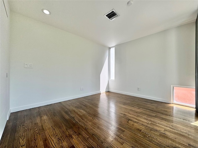 spare room with dark wood-type flooring, visible vents, baseboards, and recessed lighting
