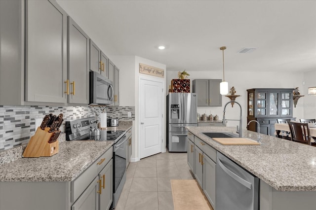 kitchen featuring appliances with stainless steel finishes, gray cabinets, decorative backsplash, and a sink