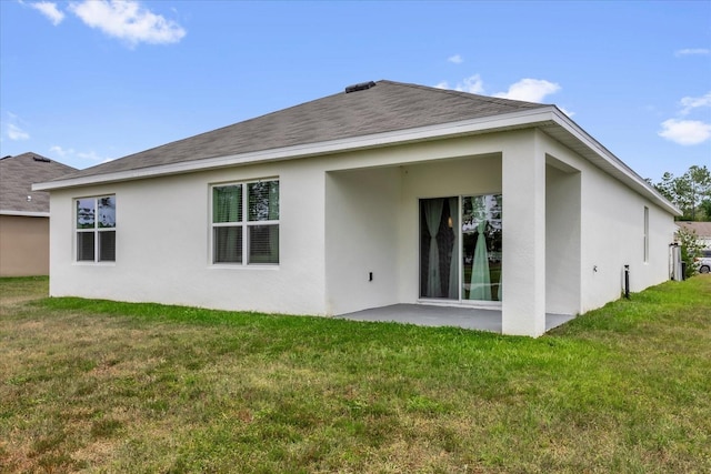 back of property with a yard, a shingled roof, a patio, and stucco siding