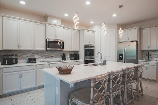 kitchen featuring a kitchen island with sink, appliances with stainless steel finishes, backsplash, a sink, and light tile patterned flooring