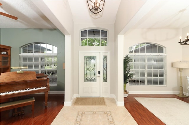 foyer entrance featuring wood finished floors, ceiling fan with notable chandelier, and baseboards