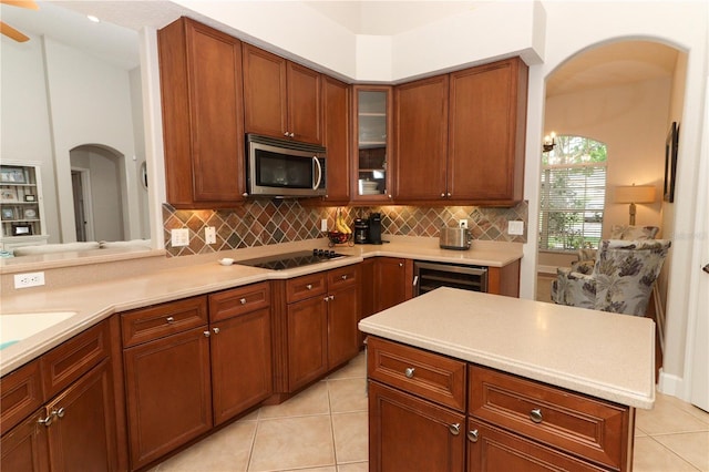 kitchen with stainless steel microwave, black electric cooktop, backsplash, arched walkways, and beverage cooler