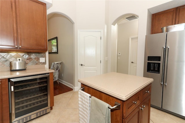 kitchen featuring light tile patterned floors, wine cooler, high quality fridge, light countertops, and arched walkways
