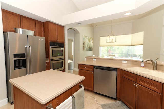 kitchen featuring arched walkways, brown cabinetry, appliances with stainless steel finishes, light countertops, and a sink