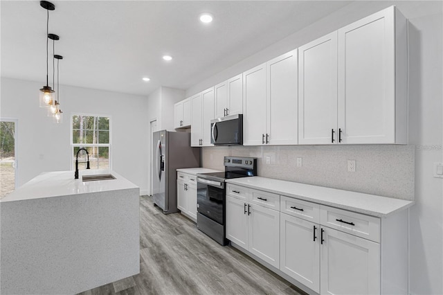 kitchen featuring decorative backsplash, white cabinets, a sink, light wood-style floors, and stainless steel appliances