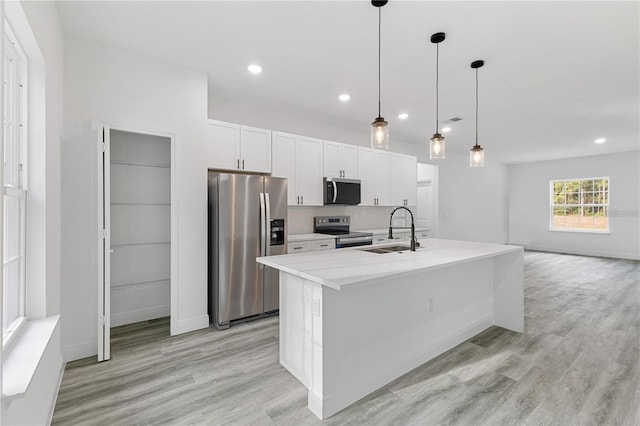 kitchen with a sink, light wood-style flooring, light countertops, white cabinets, and appliances with stainless steel finishes